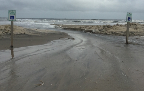 A view of the Atlantic Ocean as it floods the parking lot. The breach is between two reserved accessible parking signs.