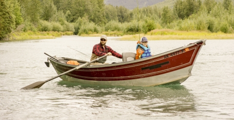 A man and a woman paddling a red boat on calm waters carrying fishing gear