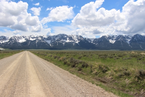 A gravel road leads toward snowy mountains with a mix of blue skies and white clouds.
