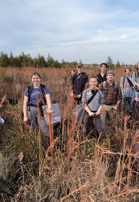 A group of people stand smiling in tallgrass outside