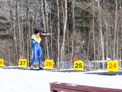 Member of the Massachusetts National Guard Biathlon Team stands in a shooting lane aiming at targets. 