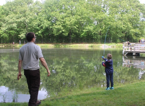 Service employee in refuge browns watches as young boy casts fishing pole into pond.