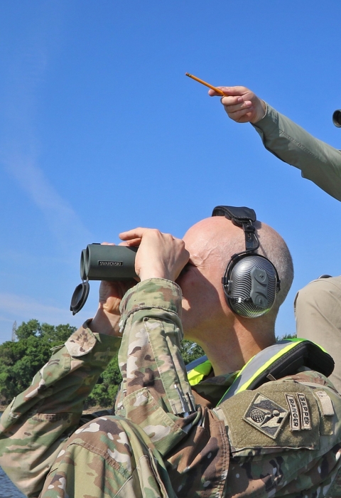 2 men sitting in boat using binoculars, using headphones