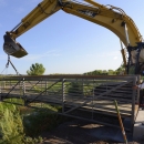 A crane operator lowers a bridge into place while a coworker on the ground adjusts the placement. 