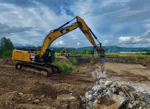 Heavy equipment on a dirt landscape with green vegetation and blue skies above