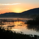 Sunset behind mountains that overlook a marsh framed by low vegetation. 
