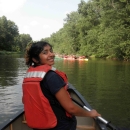 A latina woman wearing an orange personal flotation device canoeing on a river