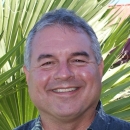 Photo of man in blue and white Hawaiian shirt with palm frond in the background.