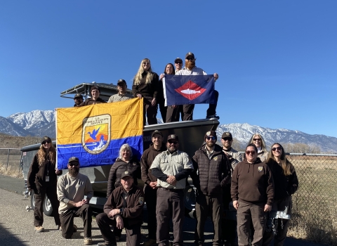 FWS staff on and around boat on trailer on land hold FWS flag, fish pennant 