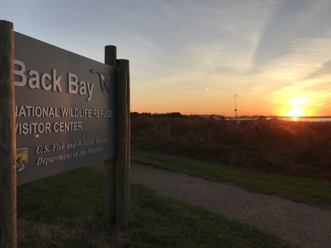 Back Bay National Wildlife Refuge entrance sign with a sunset in the background.