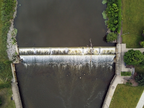 Aerial view of a dam in a dark river with green grass on both side