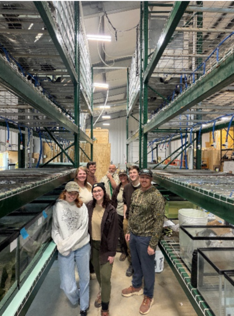 Staff stand amongst tall metal racks and fish tanks, smiling at the camera.