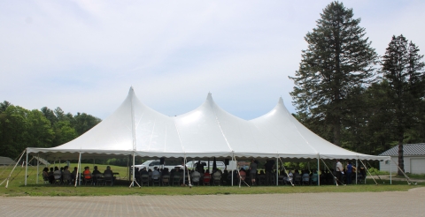 A large white tent is filled with people sitting in chairs.