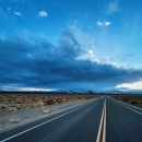 An empty road heads into the distance while dark, ominous clouds fill the sky above