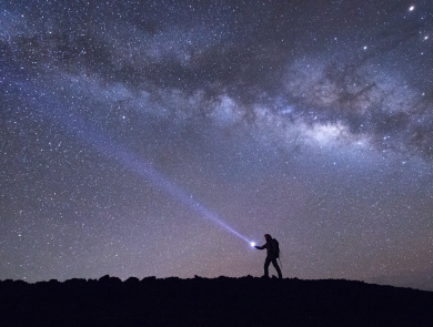 The silhouette of a hiker walking with the night sky illuminating them 