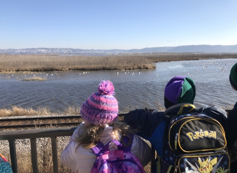Students in winter gear stand in front of a railing over looking the Mississippi River