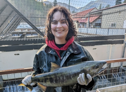 WaterCorps Service Member holding an adult chum salmon. Fish hatchery and skyline in the background.