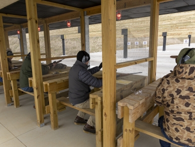 People sitting on wooden benches holding firearms and shooting at a range