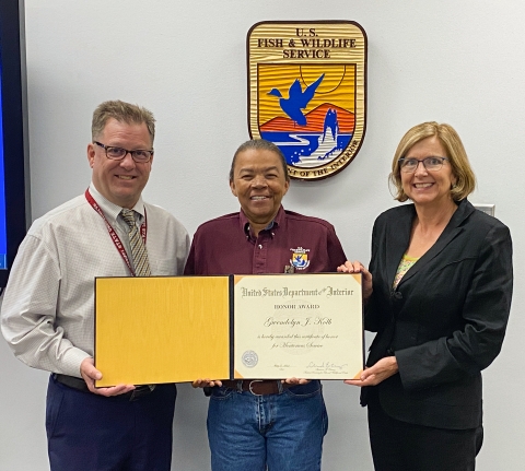Three people pose holding an open award certificate, with a U.S. Fish and Wildlife Service shield in the background.