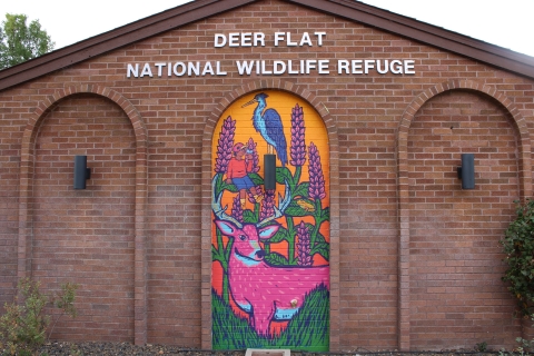Colorful mural of a deer, boy and heron on a brick building that reads "Deer Flat National Wildlife Refuge"