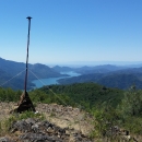 A tall pole on the top of a mountain with a microphone at the top. This pole is secured with anchors to the rocks below. In the background is a bright blue river flowing through the valley of mountains. 