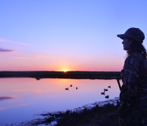 person waterfowl hunting by a wetland at sunrise
