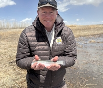 A refuge employee holding a 10" rainbow trout smiling.