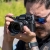 A guy with sunglasses looks through a camera lens
