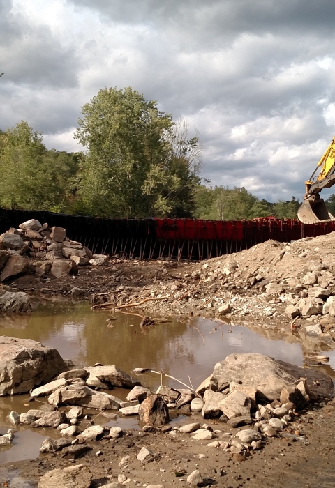 muddy, rocky riverbed with excavator on hill on right