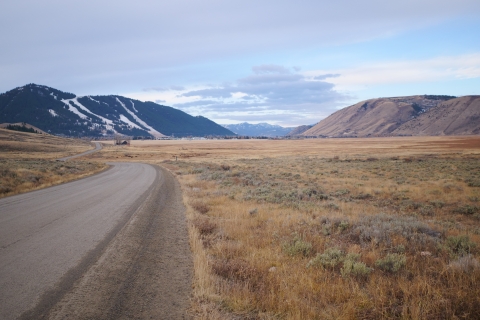 Winding dirt road across a field with mountains in the distance.