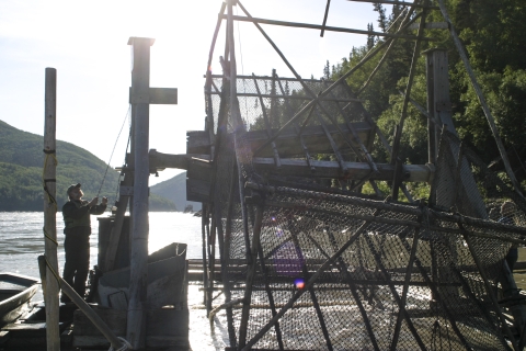 man standing on a fish wheel platform in a large river