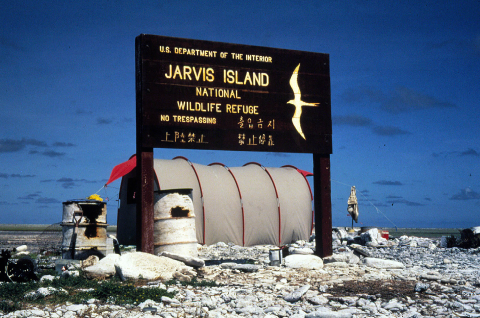 A Jarvis Island sign is posted in front of a camp site. It is wood with yellow words.