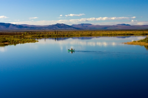 canoe crossing a brilliant blue lake with mountains in the background
