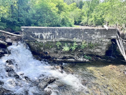 A large concrete dam spans the width of a river, allowing only a small portion of the water to flow through.