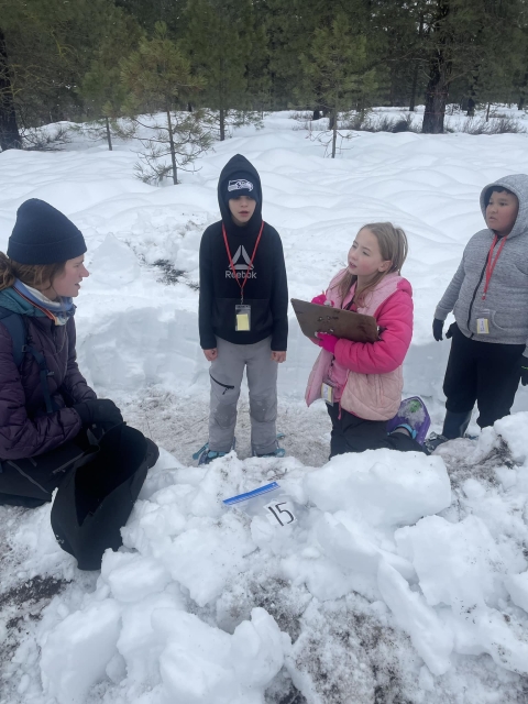 Three students stand in a snow pit with an instructor recording measurements