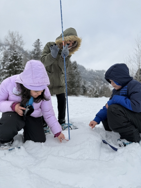Three students with a long pole in a snowy field