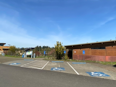 Image of three accessible parking spots with blue and white painted accessibility symbol in front of a brown building with a slanted roofline.