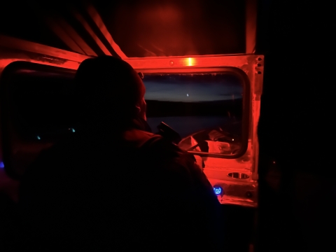 the dark shape of an officer is lit by a red tactical light in the helm of a boat
