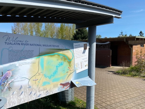 Image of a gray metal kiosk with a large map attached to it and a brown building in the background.