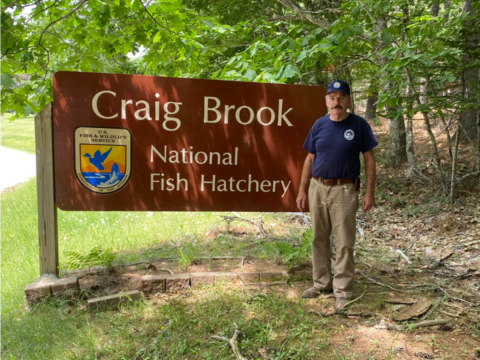 Man standing by a sign that reads "Craig Brook National Fish Hatchery."