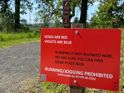A bright red sign with white and black lettering indicating that running and jogging is prohibited on the refuge trails.