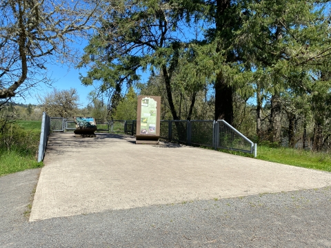 Image of a concrete pad surrounded by gray crushed gravel, with interpretive signs on it and green trees on either side.