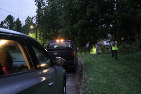 Group of people standing in the grass beside a line of parked trucks
