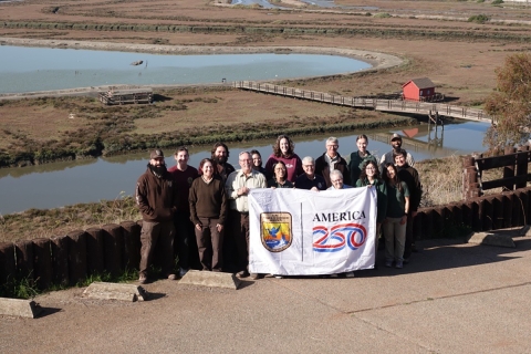 FWS staff poses with America 250 flag in front of wetland