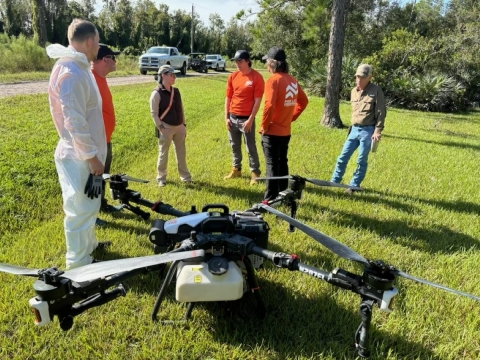 Five people stand in a semi-circle around a drone positioned on the ground