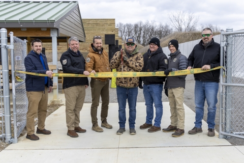 a group of people standing behind a yellow ribbon that is stretched across a sidewalk with metal gates on either side.