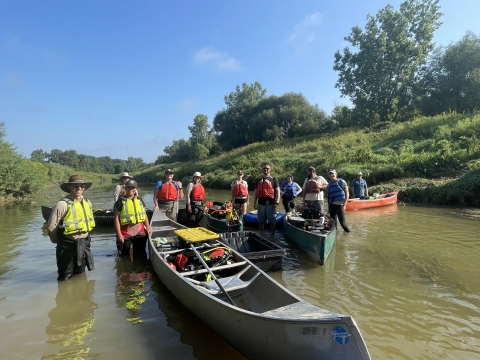 Eleven fish and wildlife staff stand in a river with four canoes.