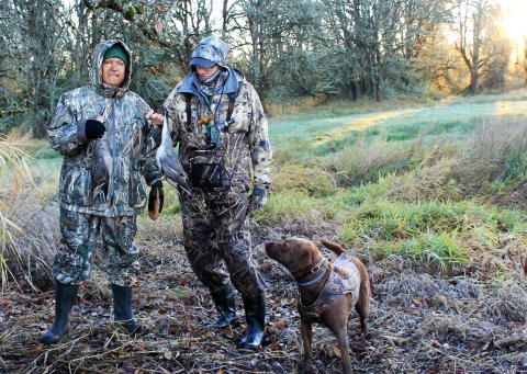 2 hunters in camo rain gear and dog