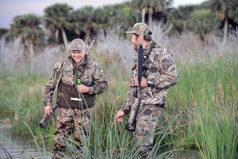 Two waterfowl hunters in camouflage wade through a wetland