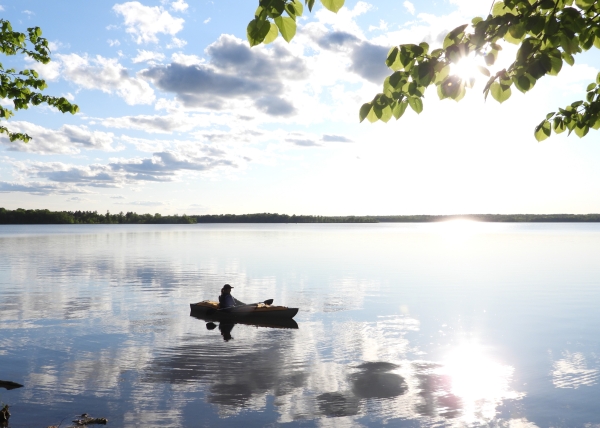 Person in kayak on lake with cloud reflections
